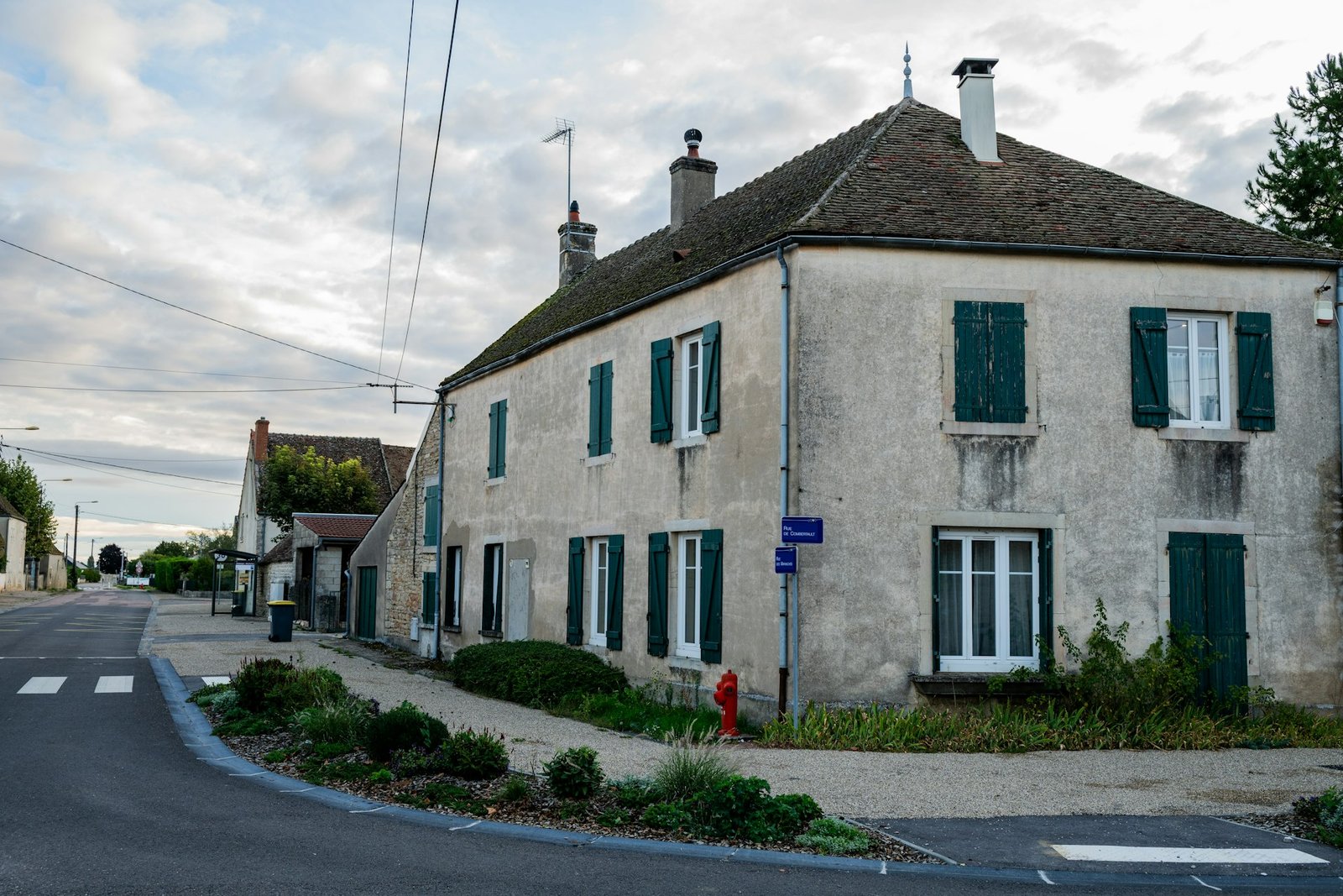 Maison à étage avec fenêtres blanches et volets battants verts sur rue